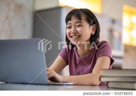 A girl in violet tshirt sitting at the laptop and looking happy A girl in violet tshirt sitting at the laptop and looking happy 93878605