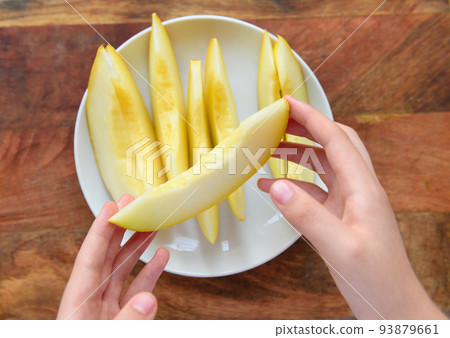 women's hands with a plate full of sliced melon on a wooden board, the concept of fresh fruit and healthy food 93879661