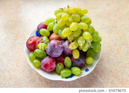 green grapes and plums in a plate on the windowsill, concept of fresh fruits and healthy food 93879670