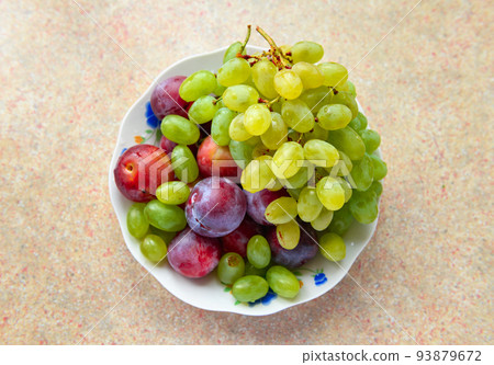 green grapes and plums in a plate on the windowsill, concept of fresh fruits and healthy food 93879672