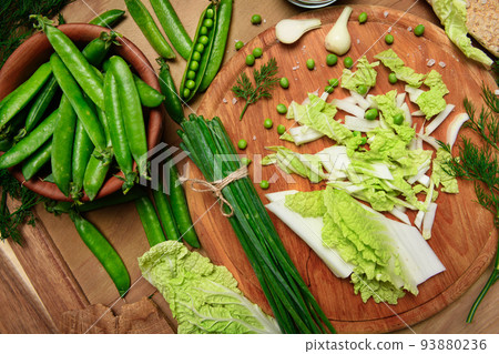 vegetables on a wooden kitchen board, green onions, dill and peas, sliced cabbage on a wood background, concept of fresh and healthy food, still life vegetables on a wooden kitchen board, green onions, dill and peas, sliced cabbage on a wood background, concept of fresh and healthy food, still life 93880236