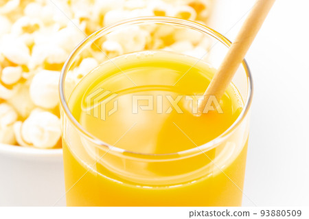 Close-up of orange juice with a paper straw. You can see the popcorn in the background. 93880509