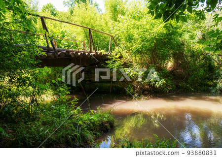 old wooden bridge over a small river in a wild forest, a beautiful summer landscape, bright sunlight through the trees reflected in the water old wooden bridge over a small river in a wild forest, a beautiful summer landscape, bright sunlight through the trees reflected in the water 93880831