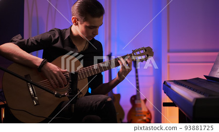 Man plays guitar. Young man plays a musical instrument. Musician records his composition in a music Studio using professional microphone Man plays guitar. Young man plays a musical instrument. Musician records his composition in a music Studio using professional microphone 93881725