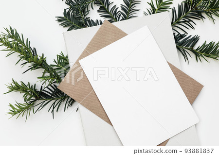 Festive closeup of Christmas blank greeting card, invitation mockup template. Craft envelope, diary and green yew tree branch isolated on white table background. Winter stationery. Flat lay, top view. Festive closeup of Christmas blank greeting card, invitation mockup template. Craft envelope, diary and green yew tree branch isolated on white table background. Winter stationery. Flat lay, top view. 93881837
