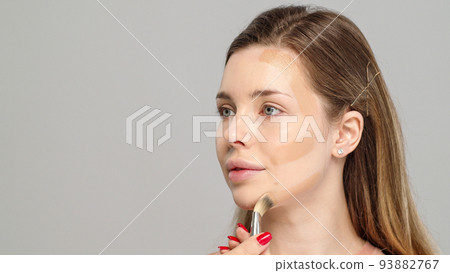 Makeup artist or stylist applies foundation or concealer to the face of the female model. Visagiste applying cosmetic foundation base on a face. Makeup artist or stylist applies foundation or concealer to the face of the female model. Visagiste applying cosmetic foundation base on a face. 93882767