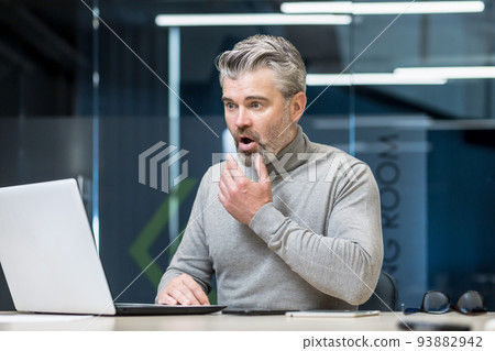 Senior gray haired businessman shocked reading bad news surprised and upset mature experienced man working with laptop inside modern office building. Senior gray haired businessman shocked reading bad news surprised and upset mature experienced man working with laptop inside modern office building. 93882942