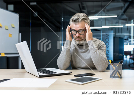Sick mature businessman working in modern office, senior experienced man having severe headache, manager massaging temples while sitting on chair, manager using laptop for work Sick mature businessman working in modern office, senior experienced man having severe headache, manager massaging temples while sitting on chair, manager using laptop for work 93883576