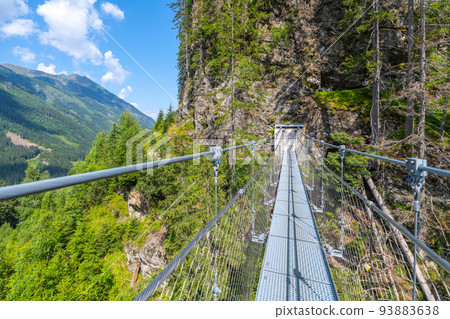 Simple suspension footbridge over mountain valley 93883638