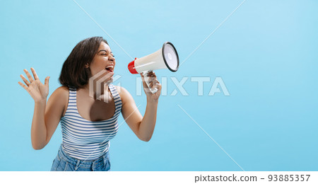 Excited young girl, student wearing casual style clothes shouting at megaphone isolated on light blue background in neon light. 93885357