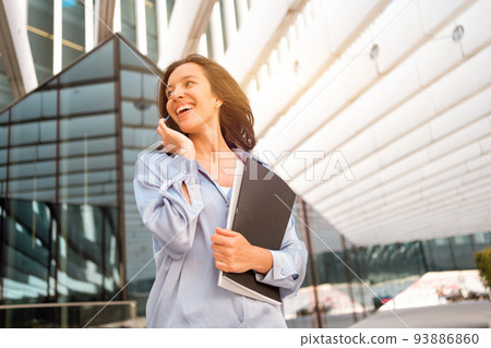 Attractive brunette businesswoman talking mobile phone with client. Pretty caucasian female business person smile when phone conversation 93886860