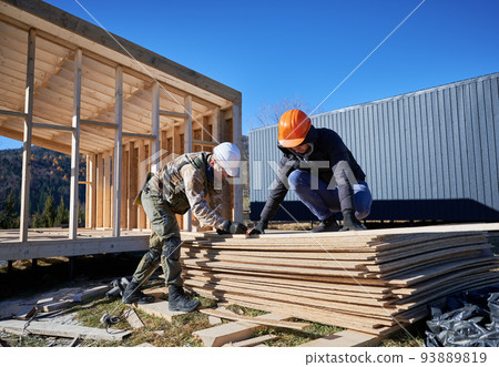 Carpenter using circular saw for cutting wooden OSB board. Man worker building wooden frame house on pile foundation. Carpentry concept. 93889819