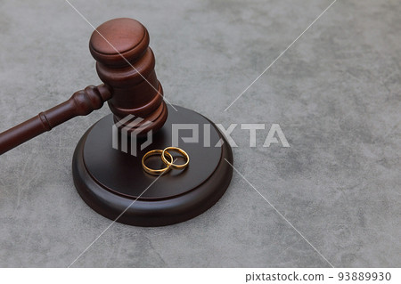 Law theme. Judge gavel wedding rings on concrete stone grey background. Divorce proceedings. Mallet of judge deciding on marriage divorce, marital agreement, legalities of divorce Law theme. Judge gavel wedding rings on concrete stone grey background. Divorce proceedings. Mallet of judge deciding on marriage divorce, marital agreement, legalities of divorce 93889930