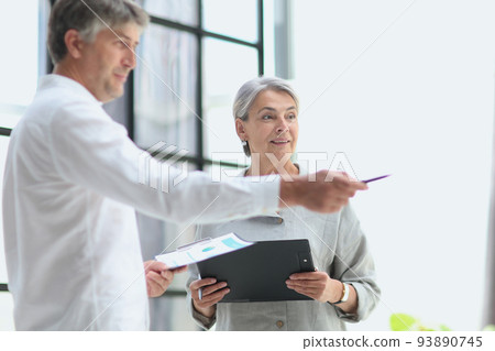 businessman showing something to mature businesswoman seen through glass 93890745
