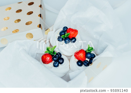 Set of Pavlova meringue dessert cakes with fresh strawberries and blueberries, decorated with mint packed in giftbox. Sweet present idea. Festive food delivery, made-to-order dessert. Selective focus. 93891140