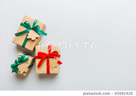 wrapped christmas or other holiday handmade present in paper with colored ribbon. Present box, decoration of gift on colourfull table, top view with copy space 93892420