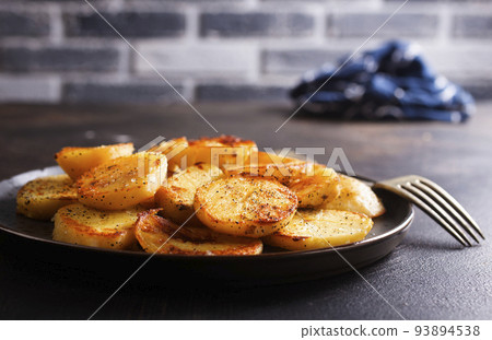 Fried potato wedges with oil, herbs on stone board Fried potato wedges with oil, herbs on stone board 93894538