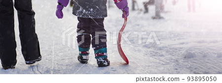 The girl is holding a red sled in her hands to ride the hill. Sledging. Activities for children and teenagers. Winter entertainment and sports. The girl is holding a red sled in her hands to ride the hill. Sledging. Activities for children and teenagers. Winter entertainment and sports. 93895050