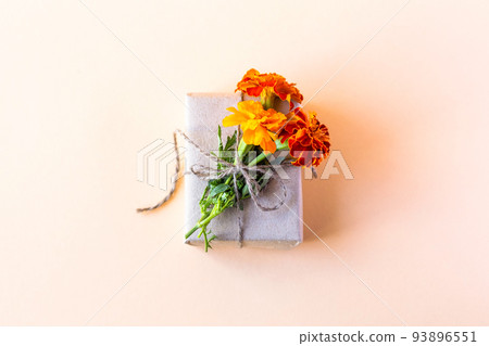 Gift box in gray craft paper decorated with orange flowers marigolds on an orange background for the holiday, flat lay 93896551