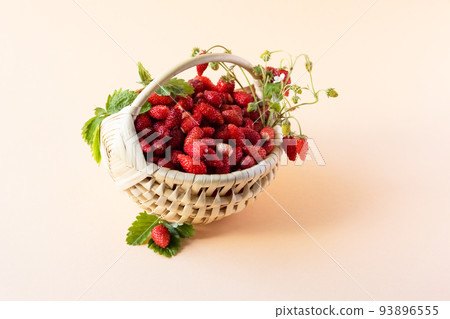 Wild strawberries in a beige basket on a orange background with green leaves, healthy and delicious food 93896555