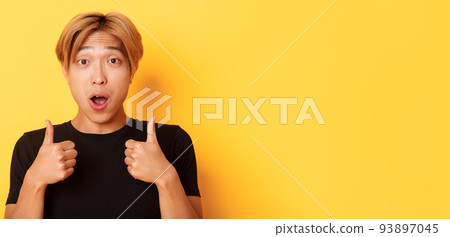 Close-up of impressed and excited handsome asian guy showing thumbs-up and looking amazed, standing over yellow background 93897045