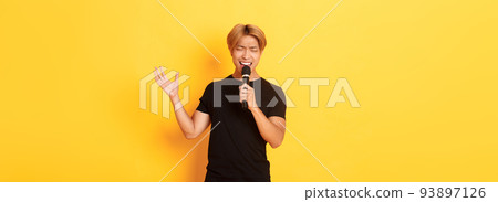 Handsome asian male singer, korean guy singing song at karaoke in microphone with passion, standing over yellow background Handsome asian male singer, korean guy singing song at karaoke in microphone with passion, standing over yellow background 93897126