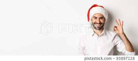 Party, winter holidays and celebration concept. Confident man in santa hat showing okay sign, approve and like, white background Party, winter holidays and celebration concept. Confident man in santa hat showing okay sign, approve and like, white background 93897128