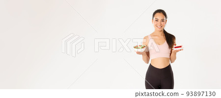 Sport, wellbeing and active lifestyle concept. Good-looking fitness coach, girl workout and staying on diet, holding plates with salad and diet, smiling, taking care of weight and calories Sport, wellbeing and active lifestyle concept. Good-looking fitness coach, girl workout and staying on diet, holding plates with salad and diet, smiling, taking care of weight and calories 93897130