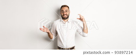 Businessman showing small gesture, looking displeased, shrugging confused, standing against white background 93897214