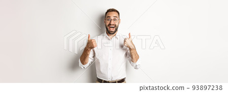 Excited man in glasses showing thumbs up and looking amazed, agree and approve something great, recommending product, standing over white background Excited man in glasses showing thumbs up and looking amazed, agree and approve something great, recommending product, standing over white background 93897238