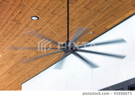 HVLS ceiling fan big fans for hot air cooling. Large ceiling fans for open air building with brown ceiling and white wall on background HVLS ceiling fan big fans for hot air cooling. Large ceiling fans for open air building with brown ceiling and white wall on background 93898073