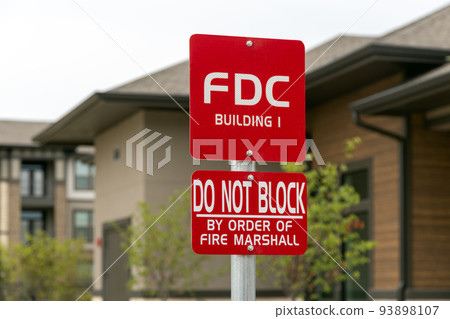 Information sign with inscription: FDC Building 1, do not block by order of fire marshal, trees and bulding on background Information sign with inscription: FDC Building 1, do not block by order of fire marshal, trees and bulding on background 93898107