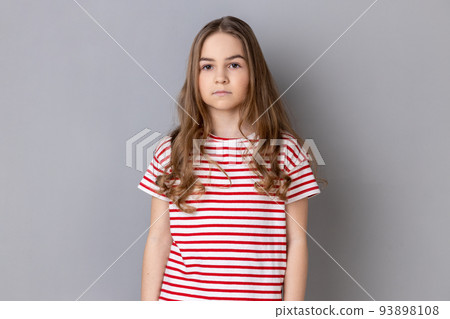 Portrait of strict serious little dark haired girl wearing striped T-shirt looking at camera with confident concentrated expression. Indoor studio shot isolated on gray background. Portrait of strict serious little dark haired girl wearing striped T-shirt looking at camera with confident concentrated expression. Indoor studio shot isolated on gray background. 93898108