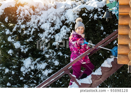 Cute adorable caucasian blond little kid girl having fun with showel enjoy climb up stairs children wooden playground covered snow cold winter day. Outdoors kid winter sport activities. warm sunlight 93898128