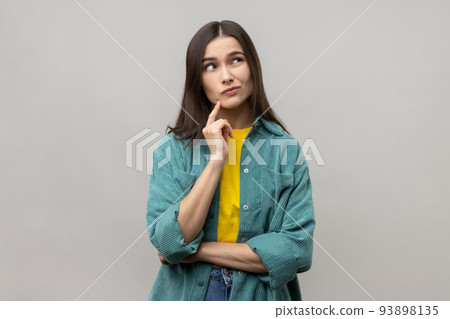 Portrait of pensive woman with dark hair thinking, looking away, having puzzled confused facial expression, wearing casual style jacket. Indoor studio shot isolated on gray background. Portrait of pensive woman with dark hair thinking, looking away, having puzzled confused facial expression, wearing casual style jacket. Indoor studio shot isolated on gray background. 93898135