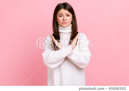 Portrait of determined brunette young woman showing x sign with crossed hands, stop, this is the end, wearing white casual style sweater. Indoor studio shot isolated on pink background. Portrait of determined brunette young woman showing x sign with crossed hands, stop, this is the end, wearing white casual style sweater. Indoor studio shot isolated on pink background. 93898303