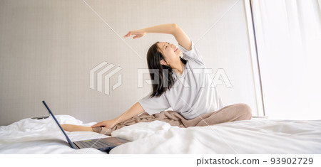 Young woman doing morning stretches while watching videos on her laptop Young woman doing morning stretches while watching videos on her laptop 93902729