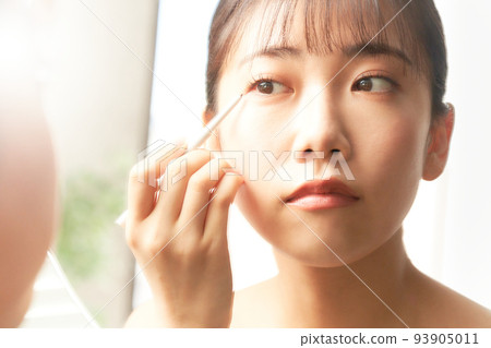Young woman doing eye makeup while looking in the mirror beauty image Young woman doing eye makeup while looking in the mirror beauty image 93905011