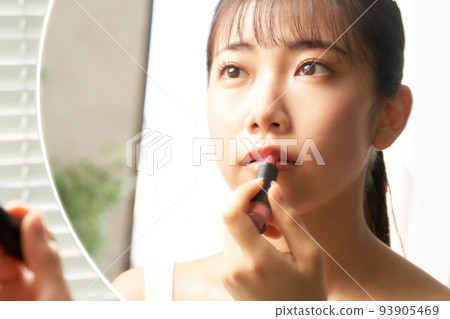Young woman applying lip while looking in the mirror beauty image Young woman applying lip while looking in the mirror beauty image 93905469