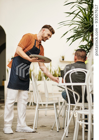Smiling waiter bringing order to customer sitting at table outdoors 93907617