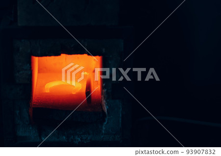Blacksmith forge oven with hot flame. Smith heating iron of steel horseshoe in fire of red-hot forge. 93907832