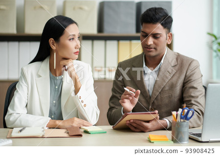 Young Indian entrepreneur asking assistant to correct some details in contract on tablet computer 93908425