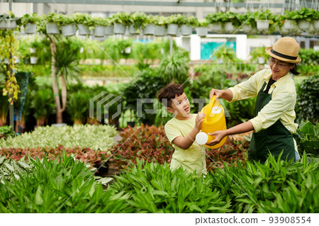 Mother showing son how to water plants at outdoors flower shop 93908554