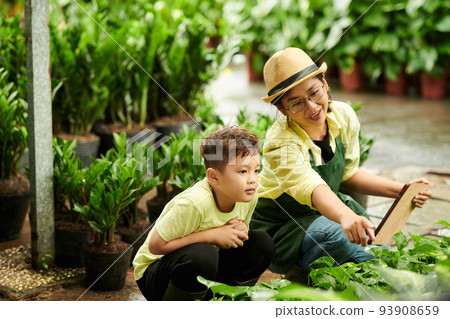 Mother working at flower nursery and teaching son how to define plants 93908659