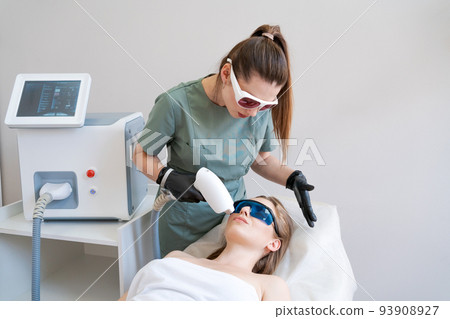 Therapist cosmetologist undergoes laser treatment on face young woman in beauty Therapist cosmetologist undergoes laser treatment on face young woman in beauty 93908927