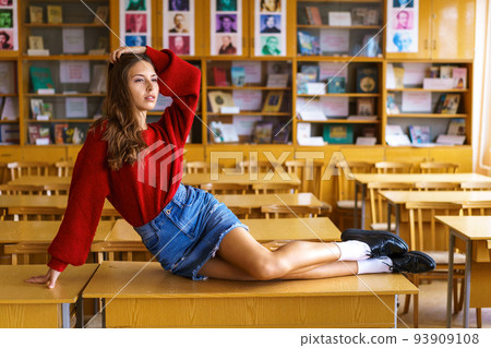 A high school student sits on a table looking seductively in a red sweater 93909108