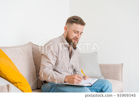 An image concentrated young bearded man sitting in notes on couch at home 93909348