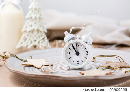 Concept Countdown on Christmas night. Table setting. Alarm clock five to twelve on a plate and christmas eco decorations on the table Concept Countdown on Christmas night. Table setting. Alarm clock five to twelve on a plate and christmas eco decorations on the table 93909966