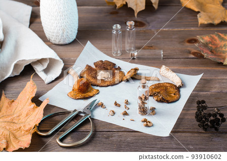 Dried chopped fly agarics stacked in a small jar and dry mushrooms on parchment and scissors on a wooden table. Microdosing and Alternative Medicine. Dried chopped fly agarics stacked in a small jar and dry mushrooms on parchment and scissors on a wooden table. Microdosing and Alternative Medicine. 93910602