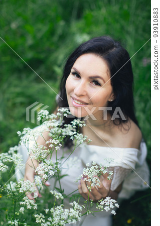 A woman in a white dress surrounded by nature and white flowers of Aegopodium podagraria. Vertical photo. A woman in a white dress surrounded by nature and white flowers of Aegopodium podagraria. Vertical photo. 93910883